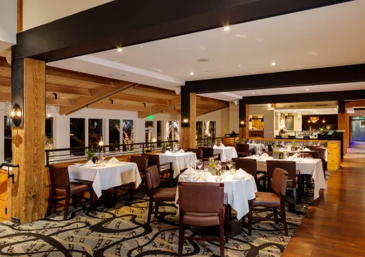 Indoor dining area with large black pillars, and leather chairs around white dining tables