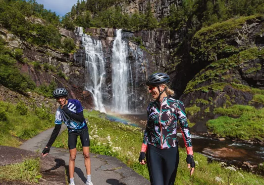 Two guests in cycling kits with a waterfall