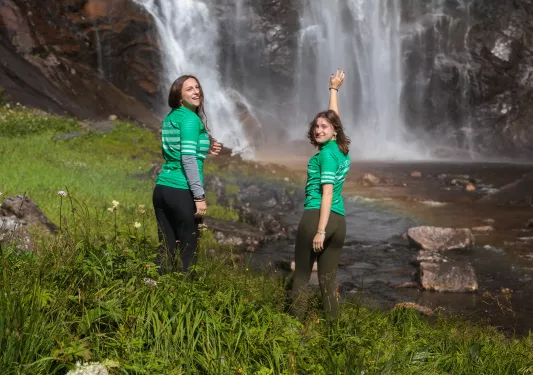 Two guests in bike jerseys pose with a waterfall
