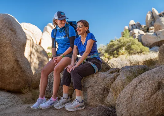 Two women smiling while sitting on large boulder on top of a mountain