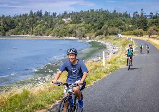 Man riding a bike on an asphalt road with a lake behind him
