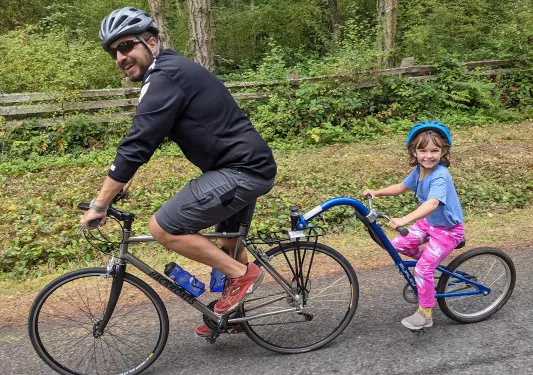 Man and a toddler riding a tandem bike on an asphalt road