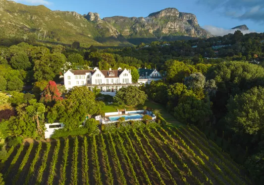 Exterior view of a white ad brown building, with a crop field and trees surrounding it
