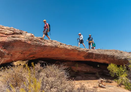 Three people hike over a rocky ledge 