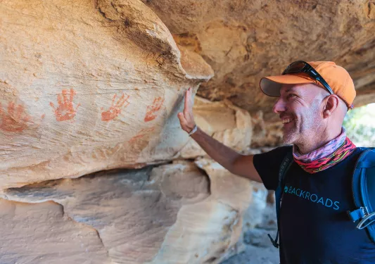 A man holds his hand up to handprints on a stone wall