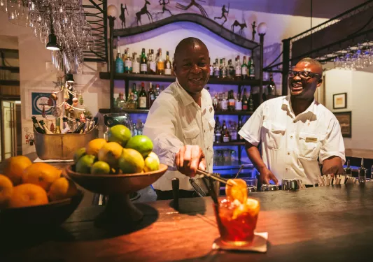 Two bartenders making alcoholic drinks and adding an orange slice to one drink