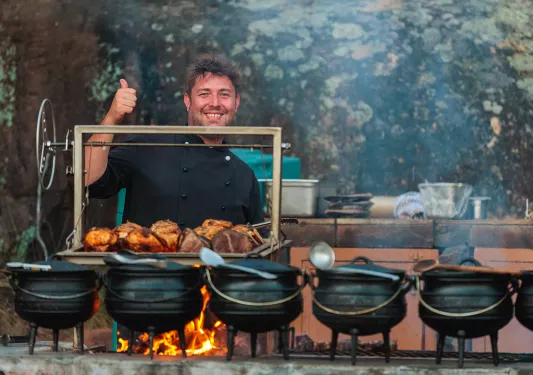 A man stands behind cauldrons of cooking food
