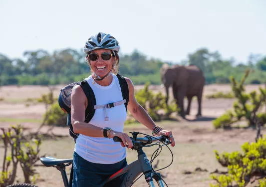 A person with a bike poses in front of an elephant