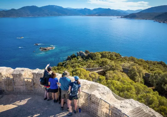 Group of men and woman on a tall rock path, overlooking to a large lake