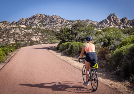 Woman riding a bike on a path going towards jagged mountains