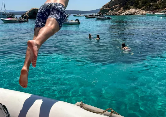 Man jumping out of a boat into a lake, with other people swimming in the ocean