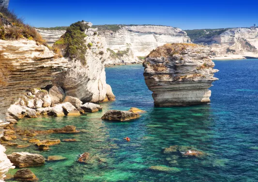 Jagged cliffs on the edge of an ocean, with a red kayak floating