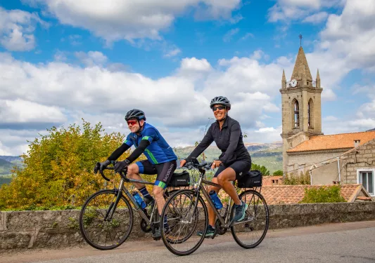 Man and woman biking on an asphalt road with a rustic clocktower in the background