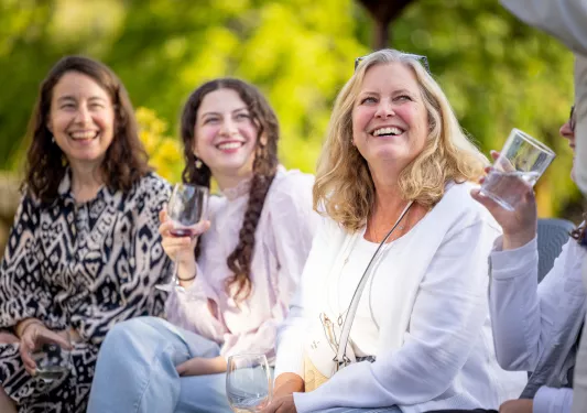 Three women smiling while looking up, holding up glasses of wine