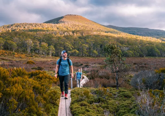 Man smiling while walking on a wooden path in the middle of a valley