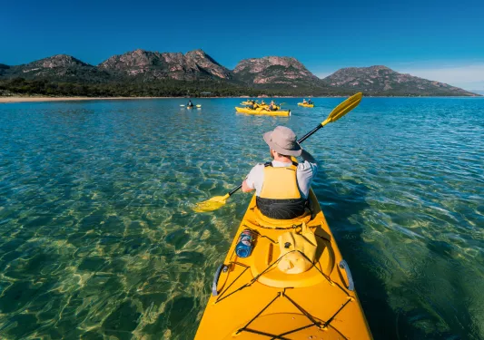 Man inside a yellow kayak paddling in the middle of a large lake