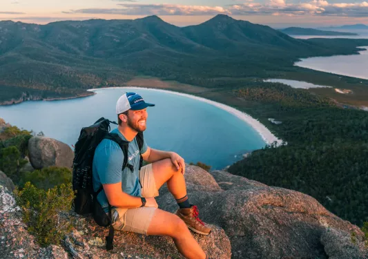 Man smiling while wearing a backpack on top of a large cliff