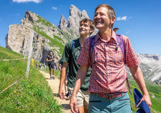 Two men smiling while looking up to the sky, while walking on a dirt trail
