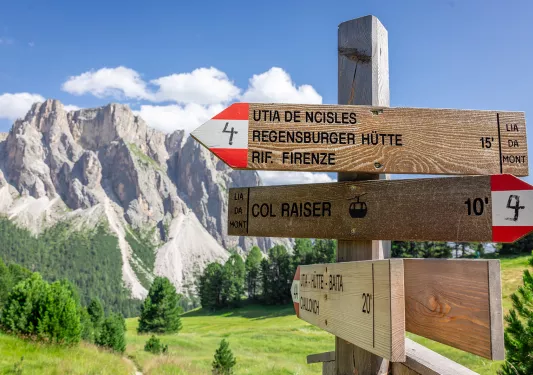 Wooden sign with red and white arrows, with tall rocky mountains in the background