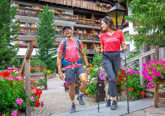 Man and women walking in a courtyard filled with flowers, while they laugh and smile