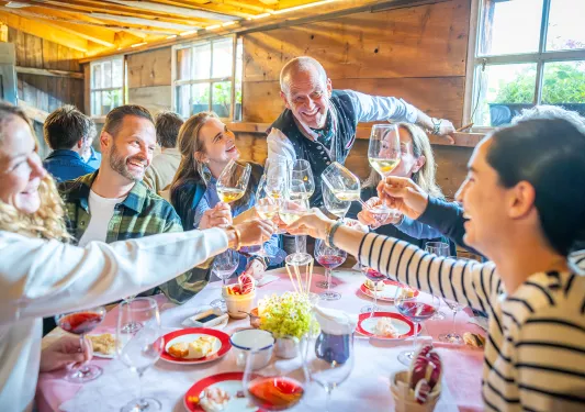Group of people around a circular table, raising their wine glasses for a toast while smiling