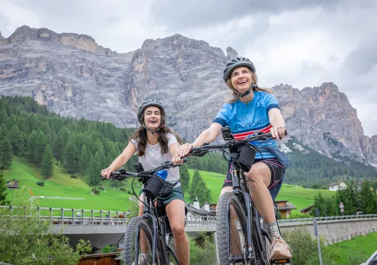 Two women smiling and riding bikes, while looking up to the sky