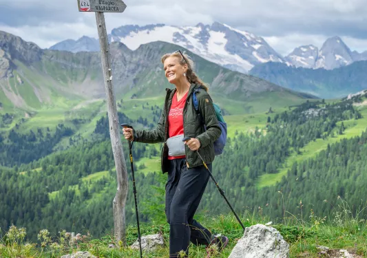 Woman smiling while holding hiking poles to ascend a grassy hill