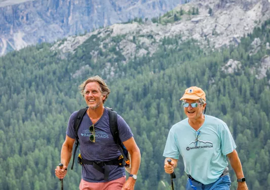 Two men smiling while ascending a gravel path with hiking poles in their hands