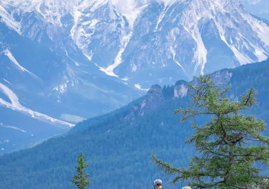 Man and woman on a dirt trail, overlooking large snow-capped mountains
