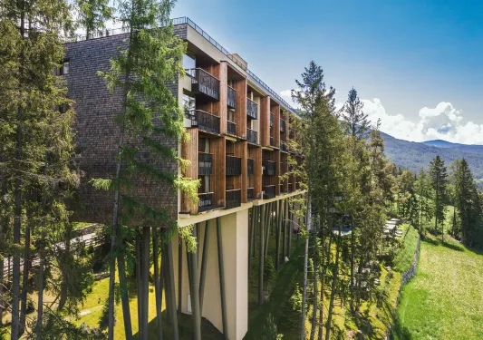 Elevated hotel building with multiple balconies overlooking a grass valley