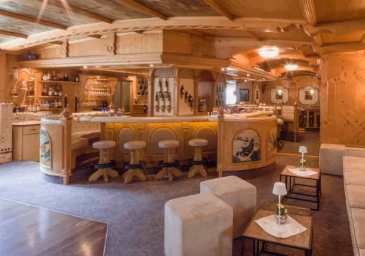 Bar in the center of a lounge with white stools and bottles of wine on the walls