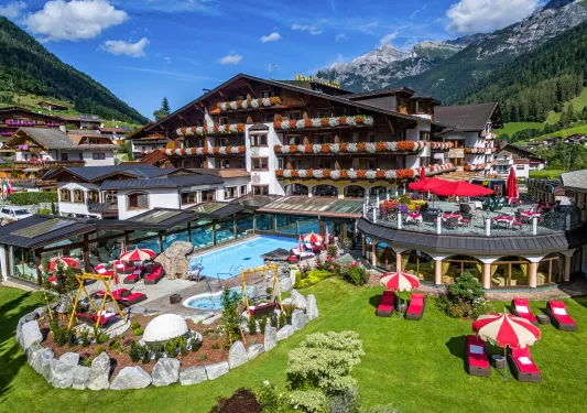 Outdoor courtyard of a large hotel with balconies, and an outdoor pool with tables and chairs surrounding