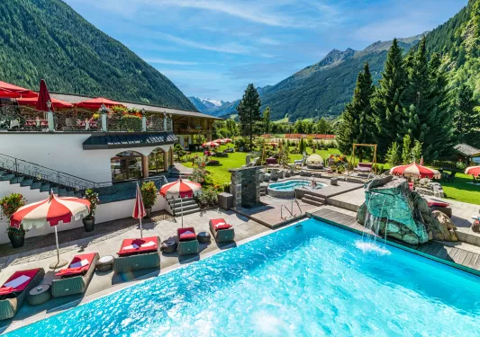 Outdoor pool with a rock fountain and red umbrellas and chairs surrounding it