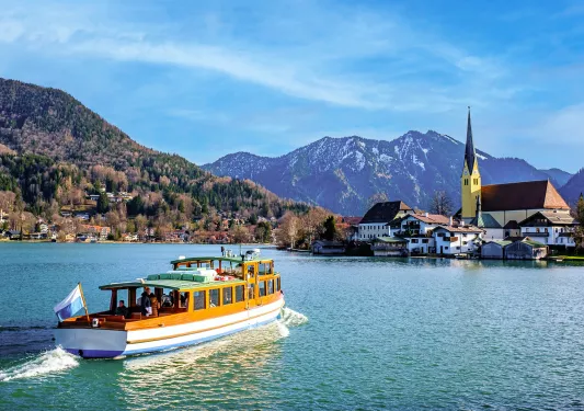 A small boat in the ocean heading towards buildings by a port