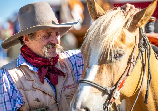 Man with a cowboy hat, while petting a horse