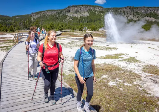 One woman and two girls hiking next to an active geyser