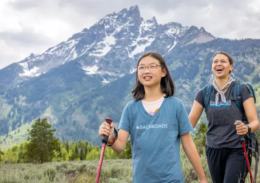 Woman and girl with walking poles hiking in a grassy valley