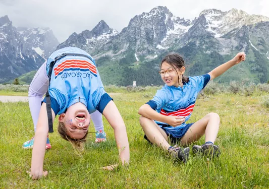 Two girls doing gymnastics in the middle of a grassy valley