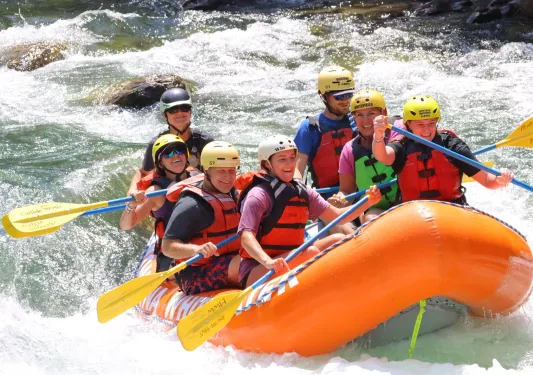 Group of men and women on an orange, inflatable raft in a river