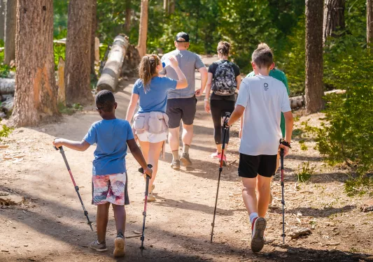 Small child and older teenager with walking sticks walking through a forest