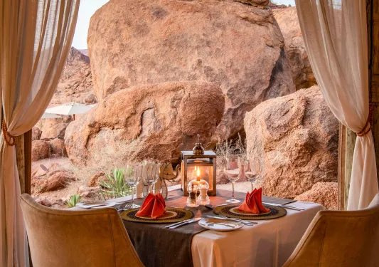 Dining table with wine glasses and a lantern with giant boulders in the background