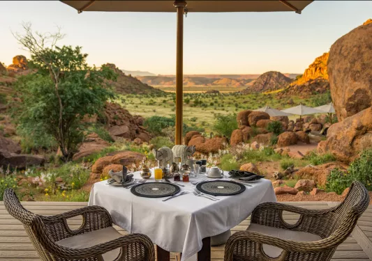 Dining table with woven chairs, looking out towards a large valley
