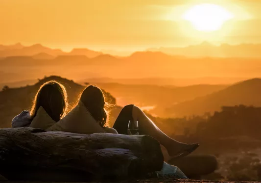 Three women sitting on a bench looking out to an open valley and a sunset