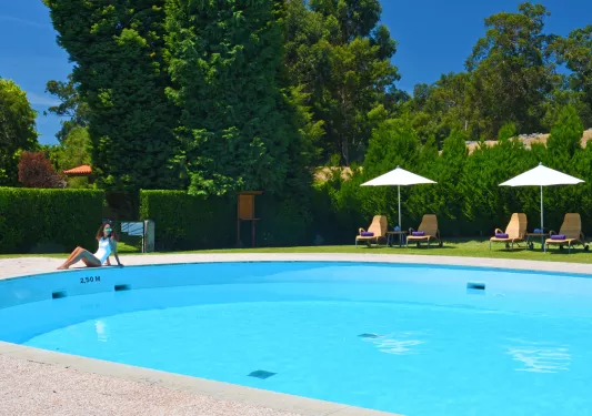 Woman sitting next to a pool, surrounded by green trees