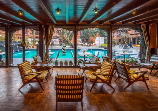 Outdoor patio with cushioned, wooden chairs looking out to an outdoor pool
