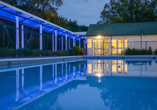 Outdoor pool with a building and covered walkway illuminated by blue and orange lights