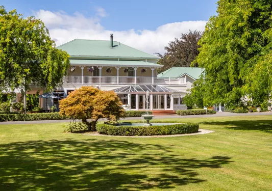 Exterior view of yellow and green building with a grass field and a fountain in the center