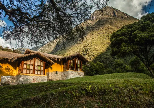 Exterior view of orange building with a straw roof, with a grassy hill in the background