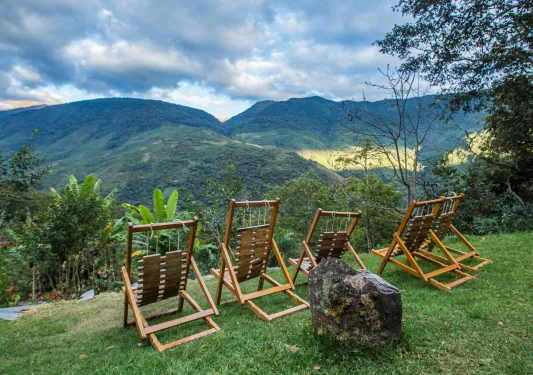 % wooden reclining chairs on a hill, looking out to grassy, tree-covered hills