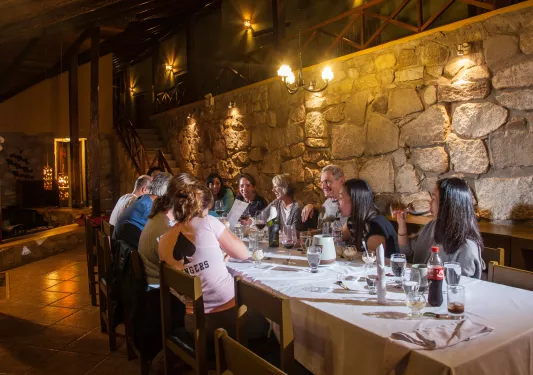 Group of people sitting on a dining table drinking wine, with a stone wall behind them